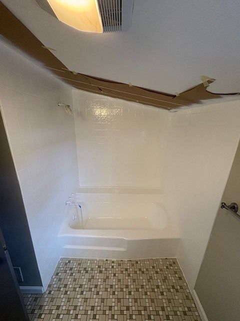 Bathroom with a damaged ceiling above the bathtub. The walls are white, the floor has a mosaic tile pattern.