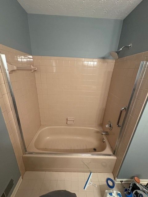 Beige tile and tub shower with a blue wall backdrop, showing a glass door, showerhead, and grab bar.