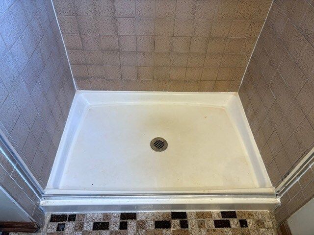 A white shower base with a drain in the center, surrounded by brown tiled walls and decorative tile at the bottom.