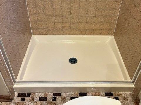 Shower stall with beige walls, a light-colored basin, and a dark drain.