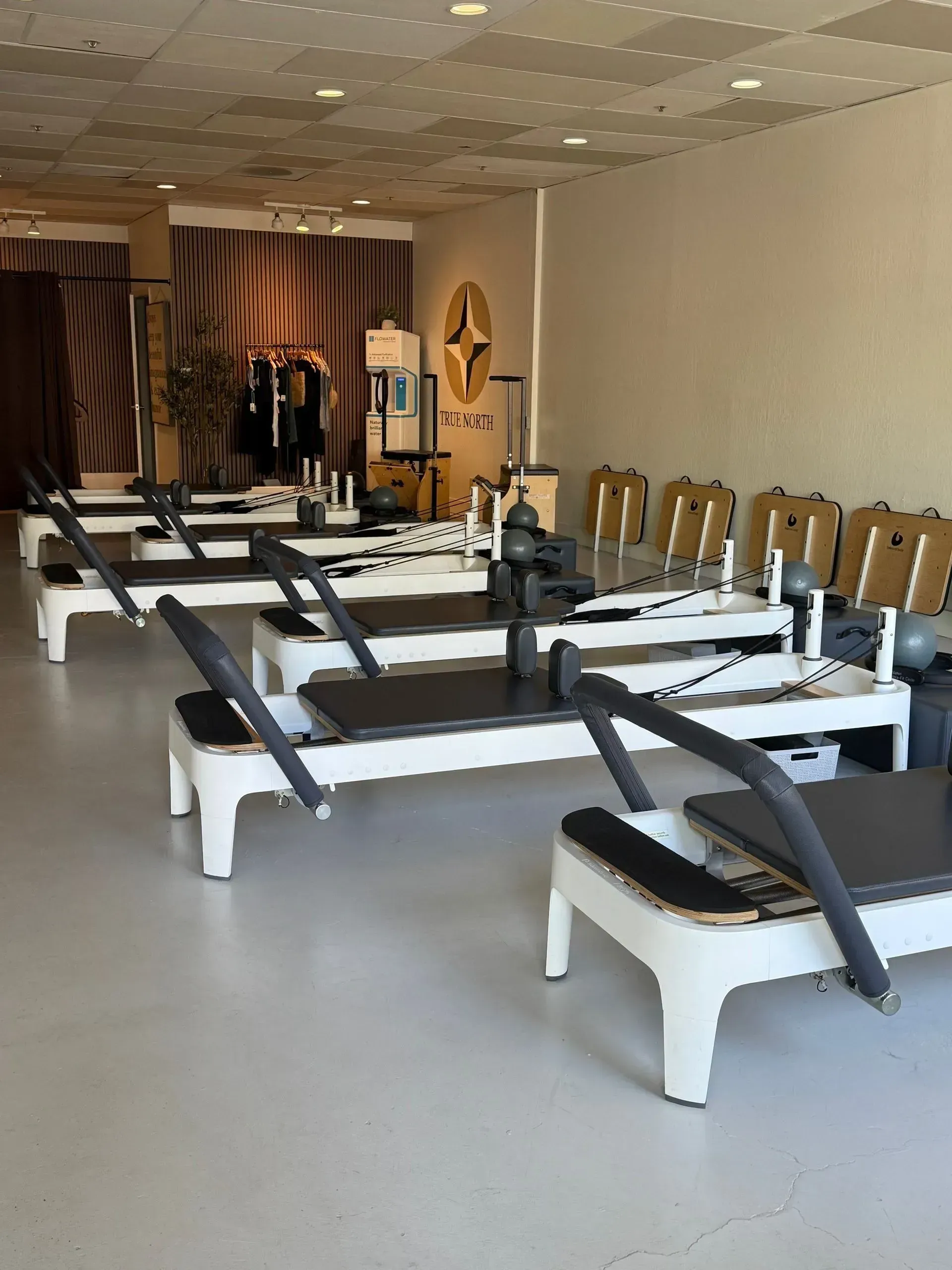Pilates reformer studio with rows of white machines and black straps in a bright room