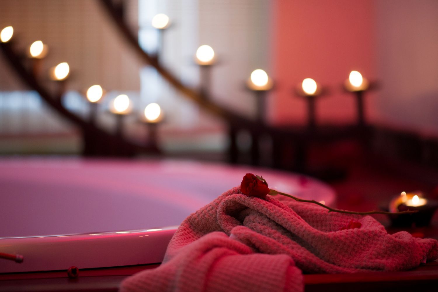 Pink towel by a bathtub with lit candles, creating a soft spa-like scene