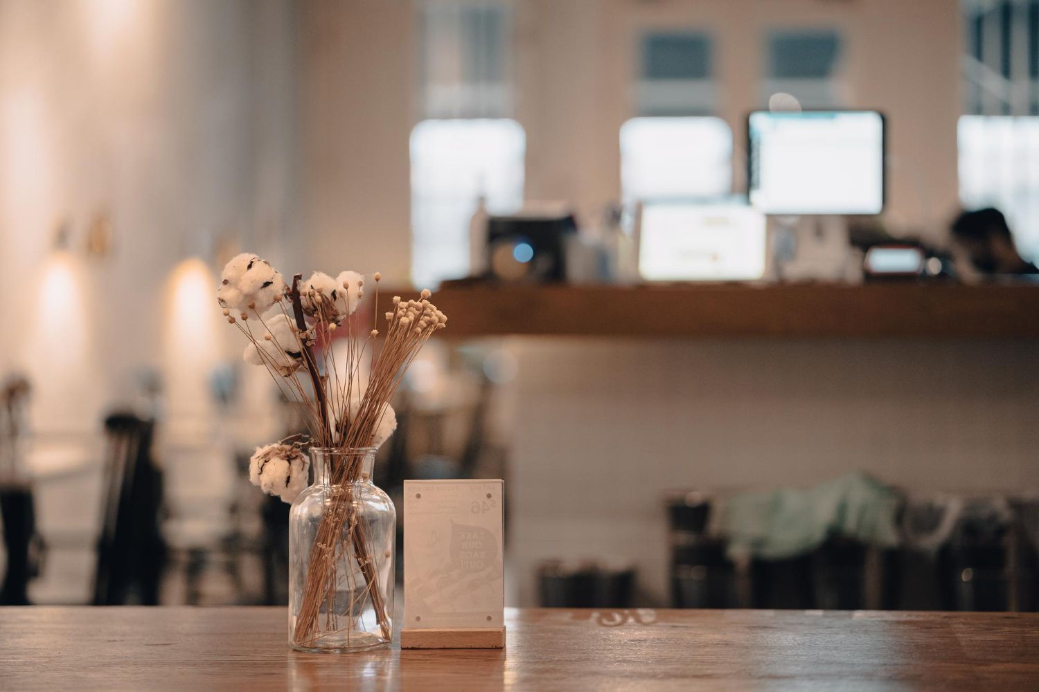 Dried flowers in a glass vase on a wooden table in a softly blurred cafe interior.