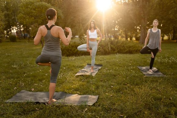Three people practicing yoga outdoors on mats in a sunlit park.