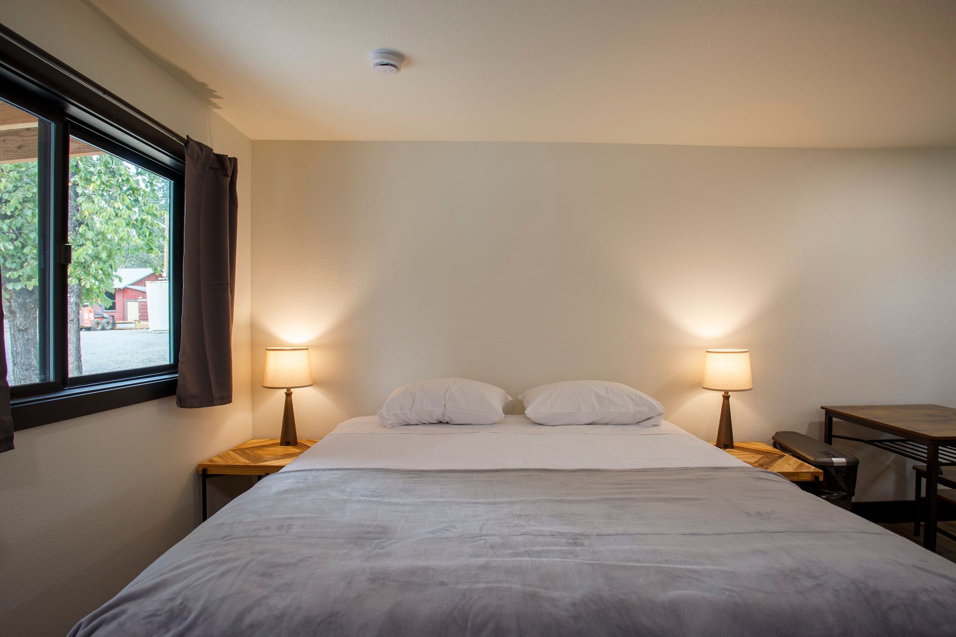 Modern bedroom with a neatly made bed, bedside lamps, and a window on the left.
