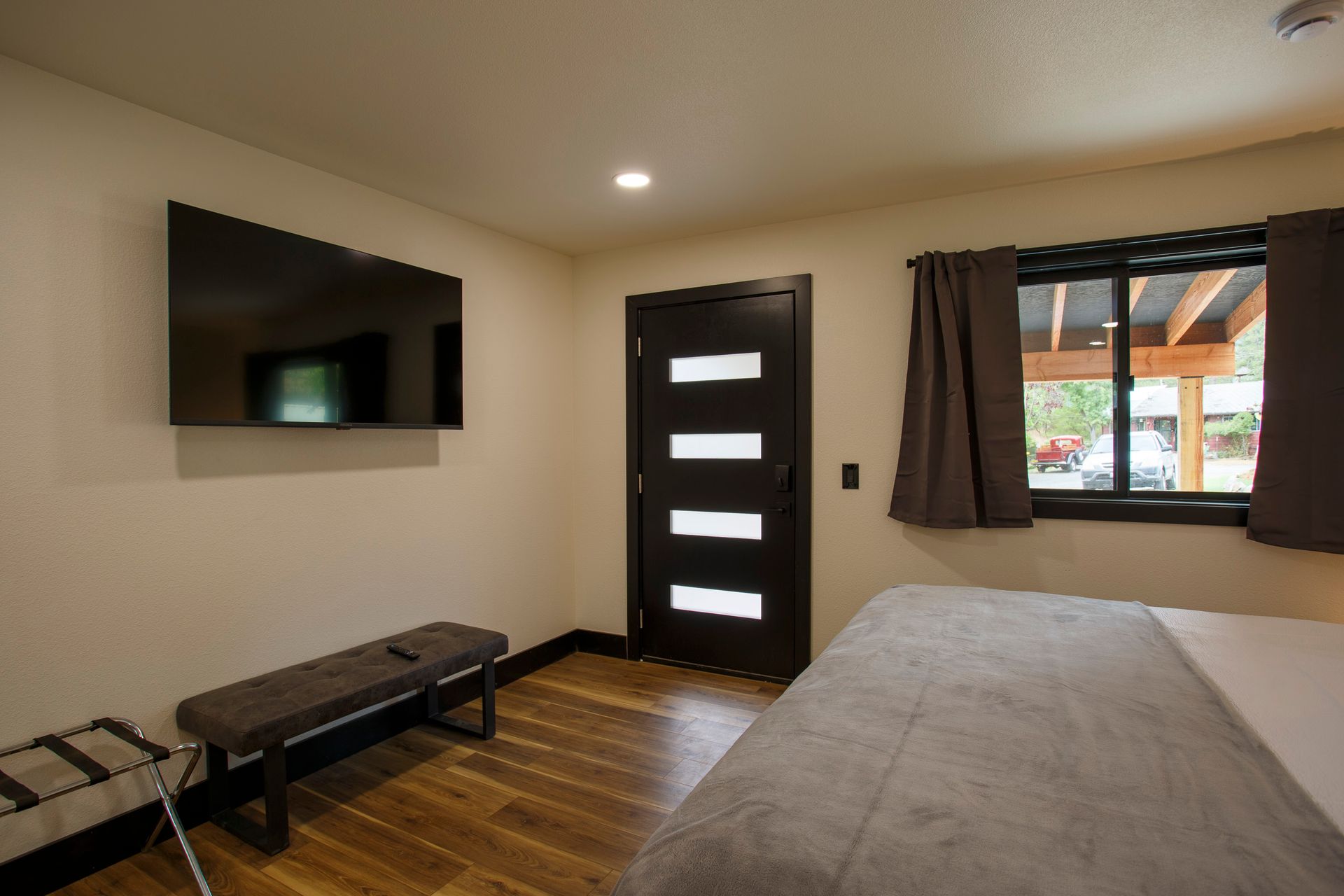 Modern bedroom with wall-mounted TV, black door, window, and neatly made bed