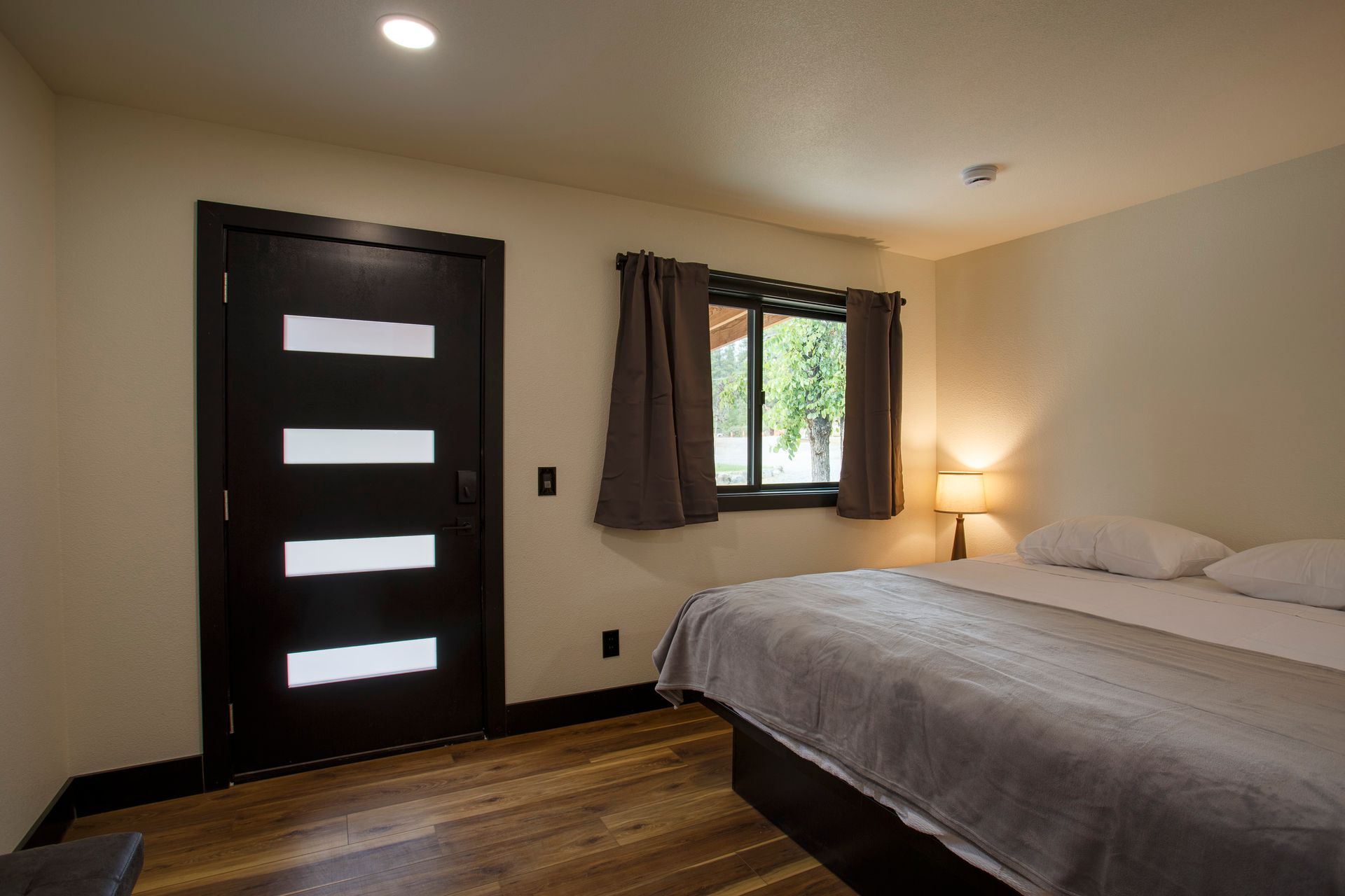 Bedroom with dark door, window, bedside lamp, and neatly made bed