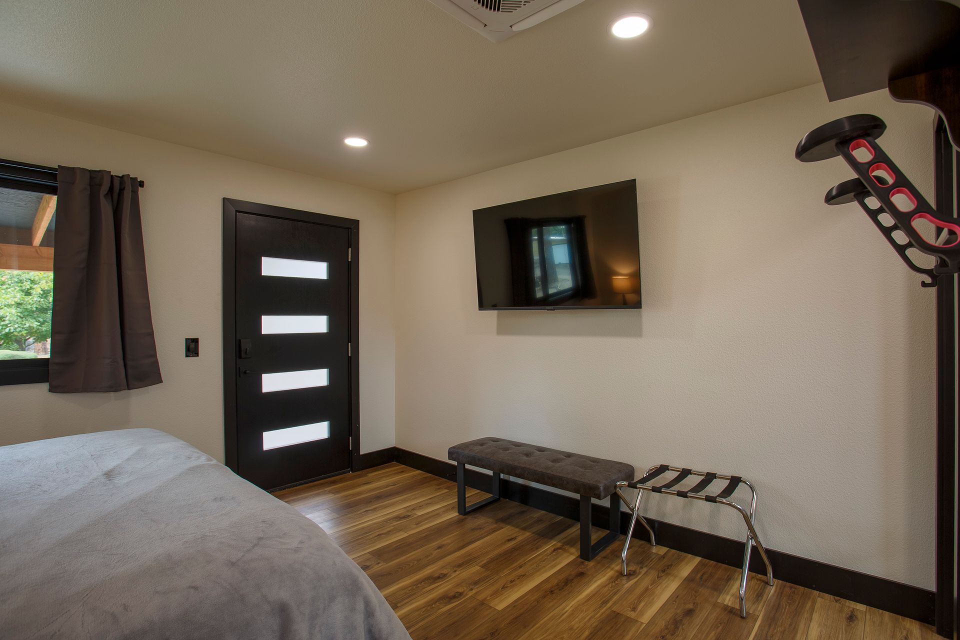 Modern bedroom with bed, wall-mounted TV, black door, and wooden floor.
