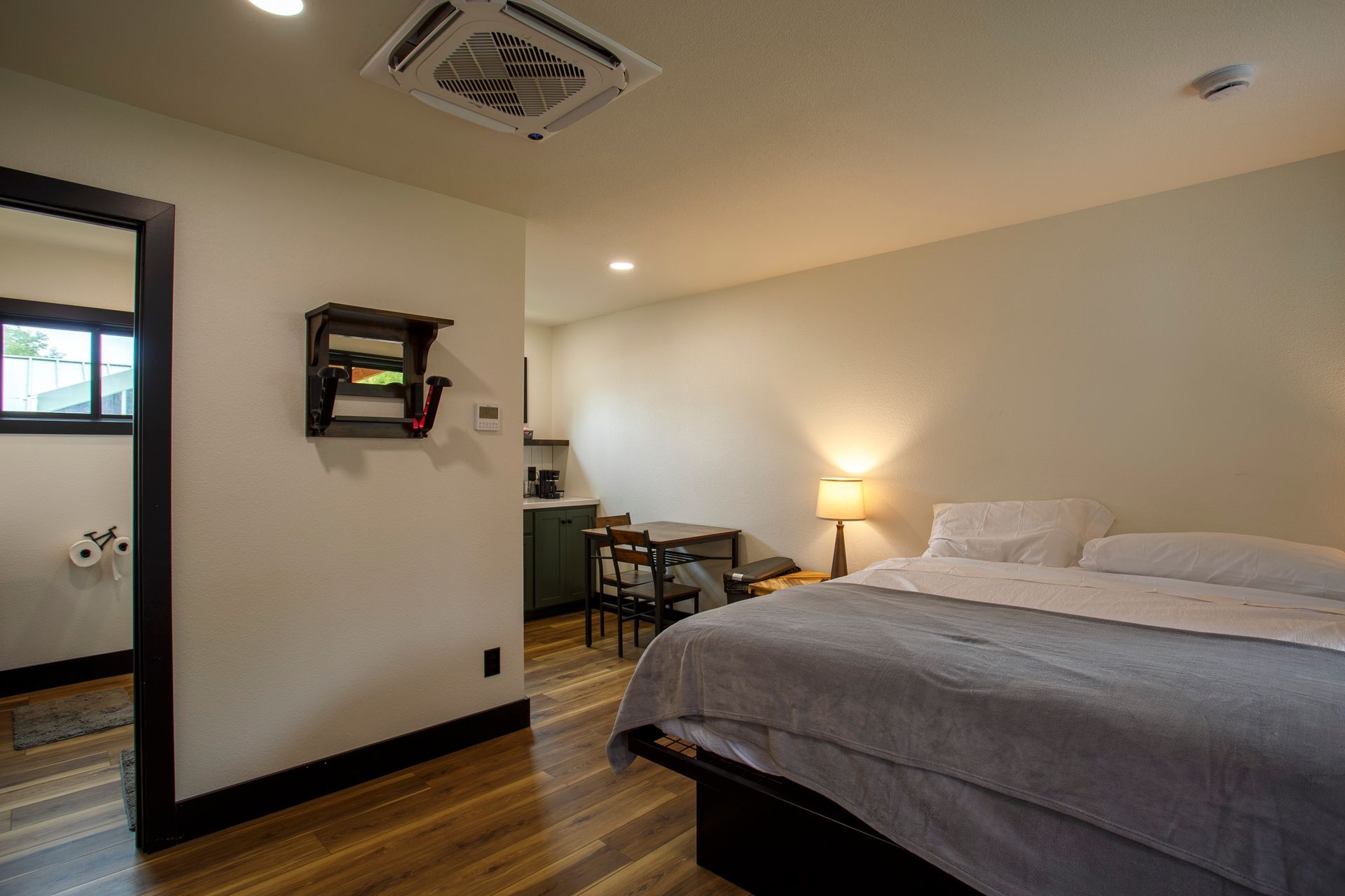 Modern bedroom with a bed, lamp, desk, and attached bathroom view