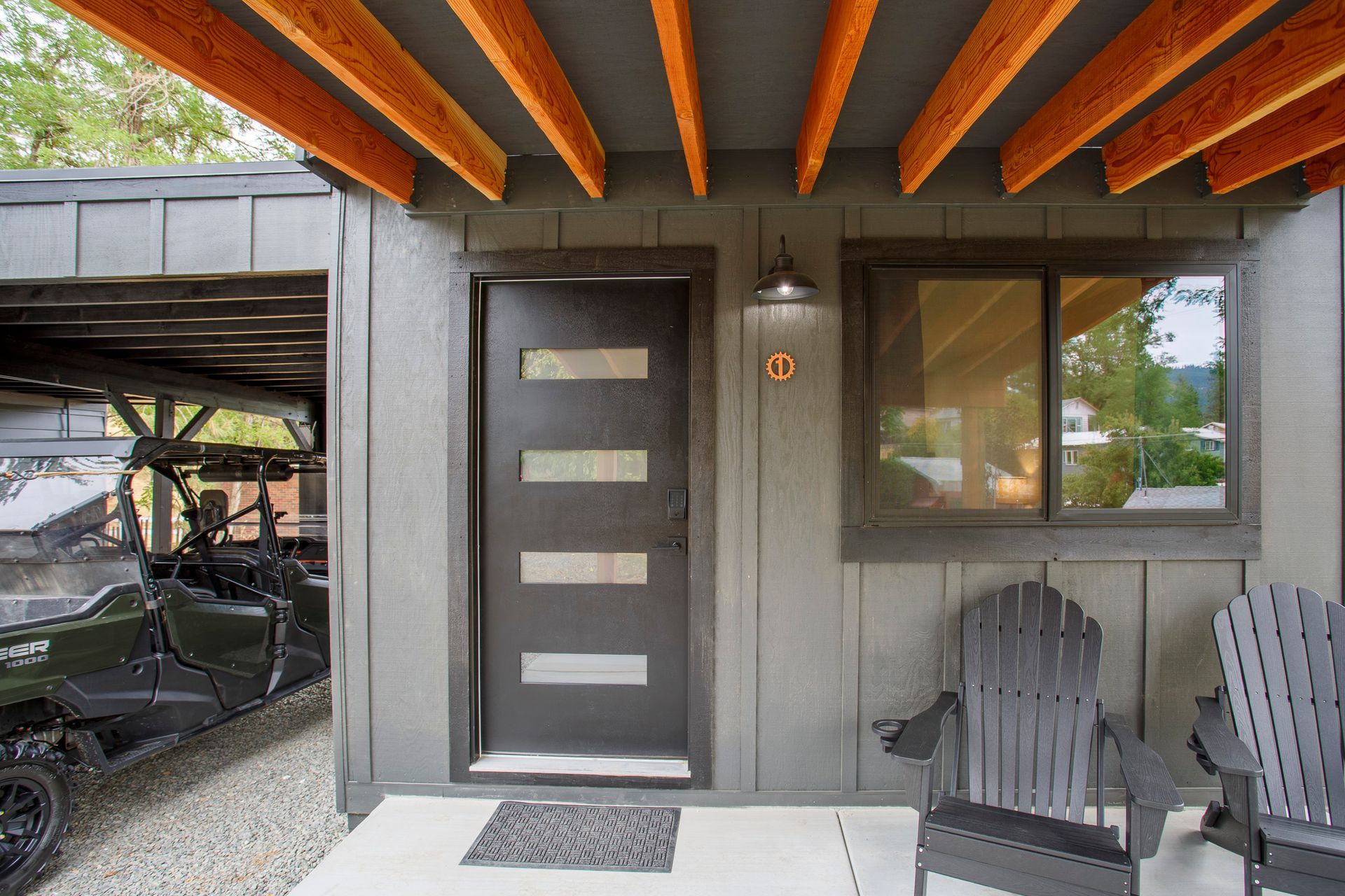 Covered patio with a modern front door, window, and two Adirondack chairs beside a garage opening