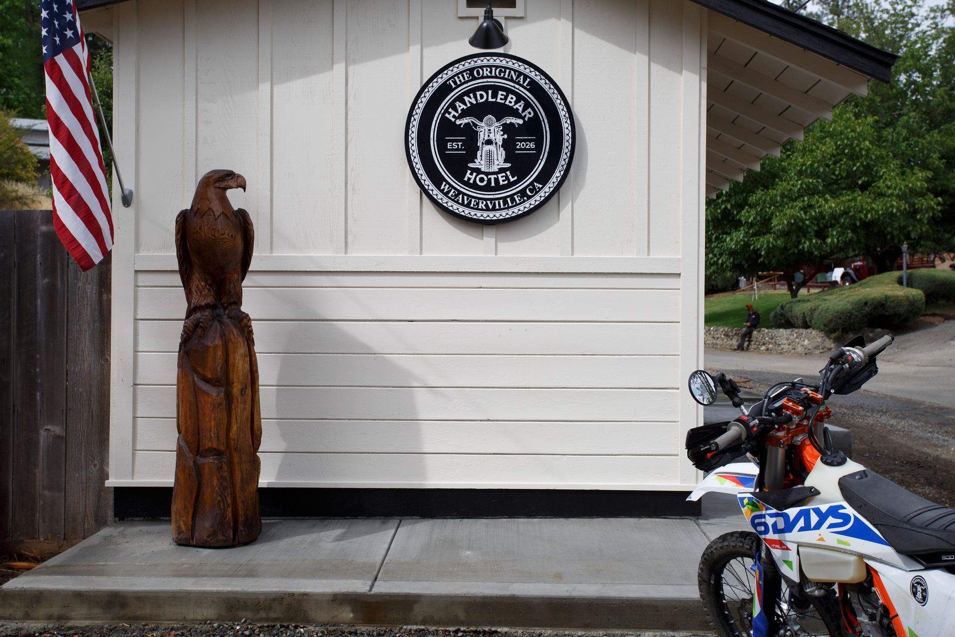 Wooden eagle statue beside a white building with a round seal and a parked motorcycle under an American flag