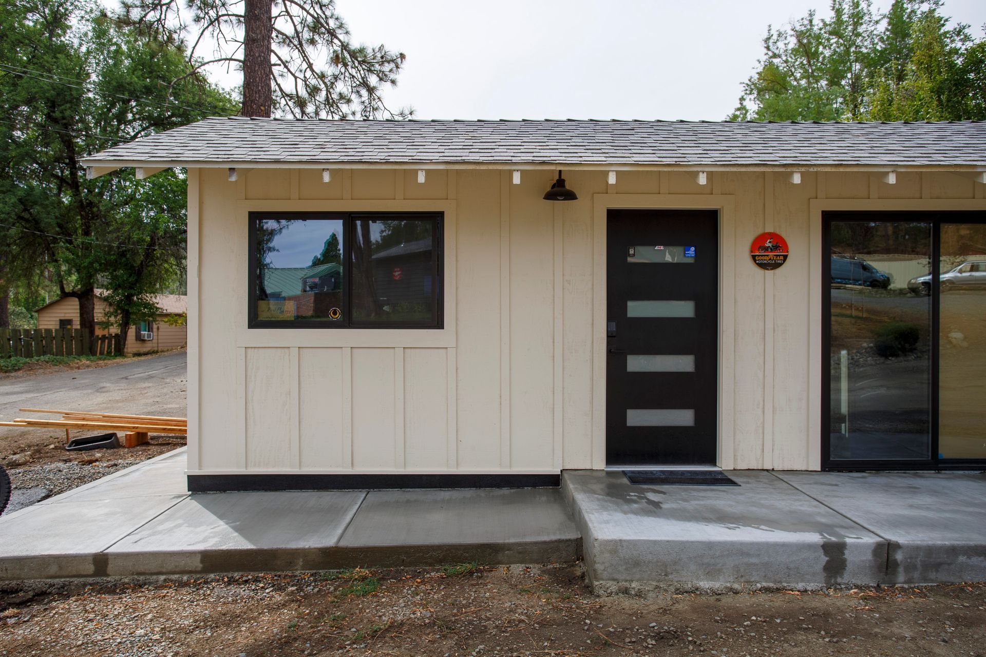 Front entrance of a beige house with black doors, windows, and a concrete walkway under construction