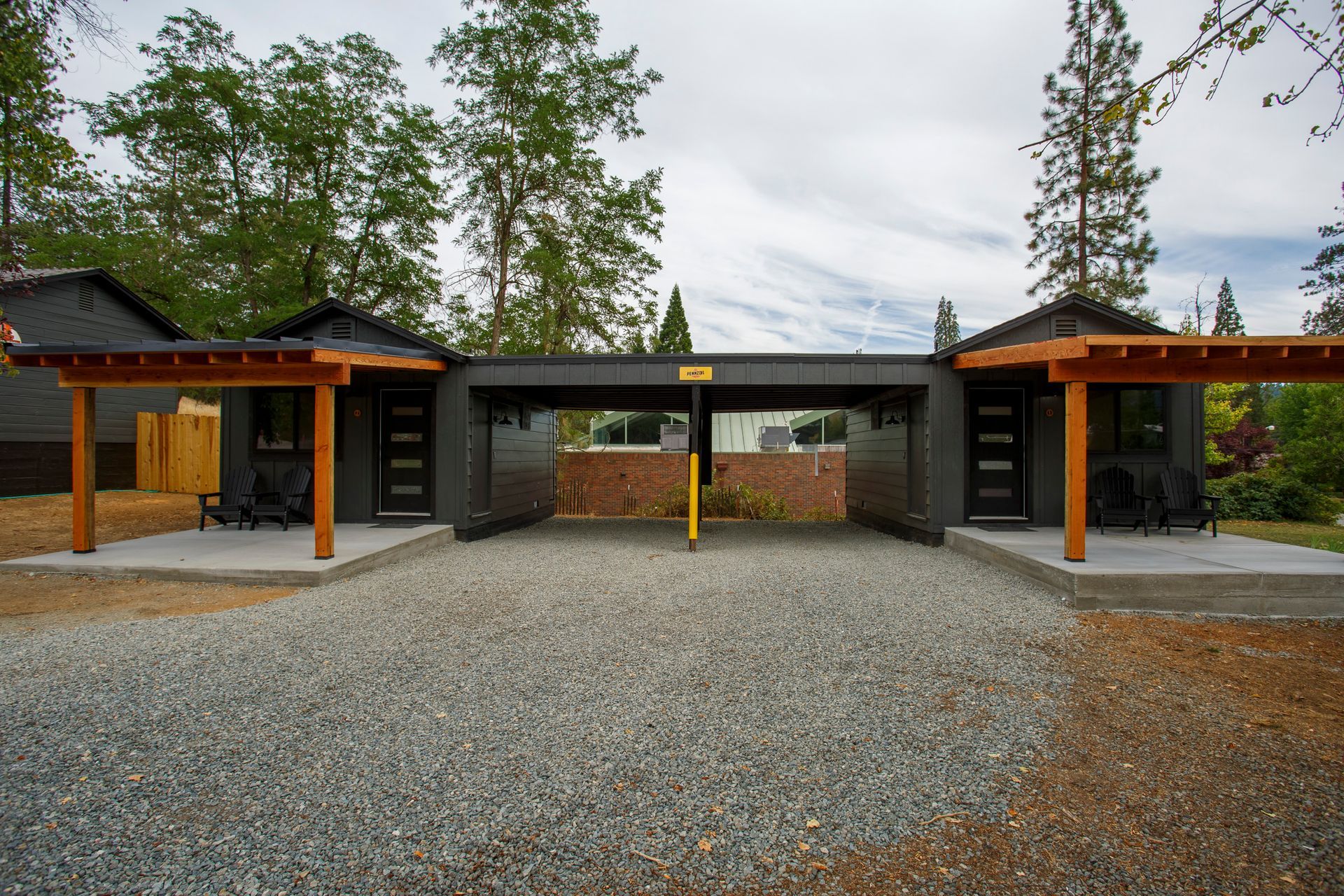 Modern gravel courtyard with open-sided wooden structures and trees in the background