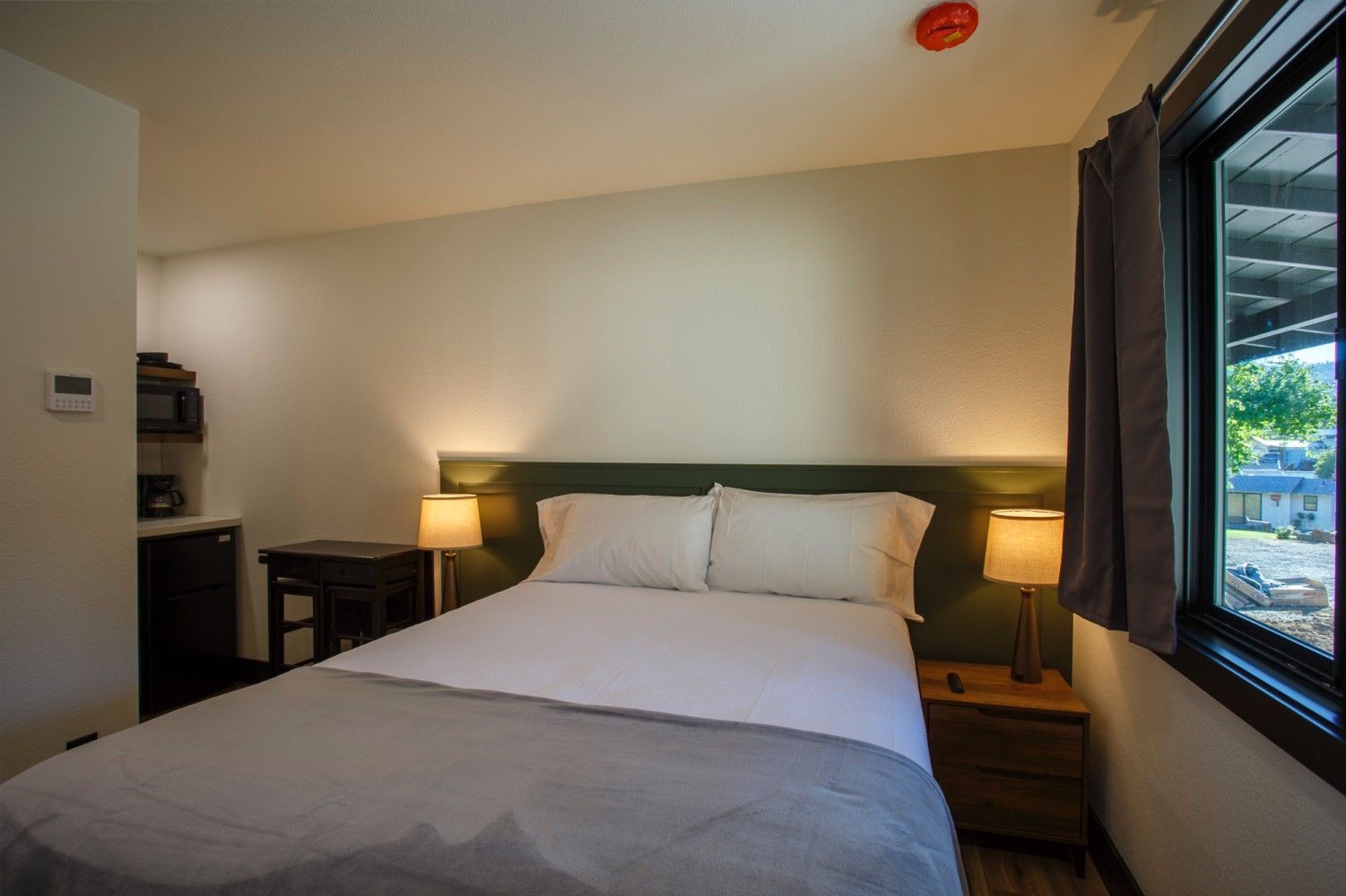 Minimal hotel bedroom with a bed, bedside lamps, and a large window overlooking greenery