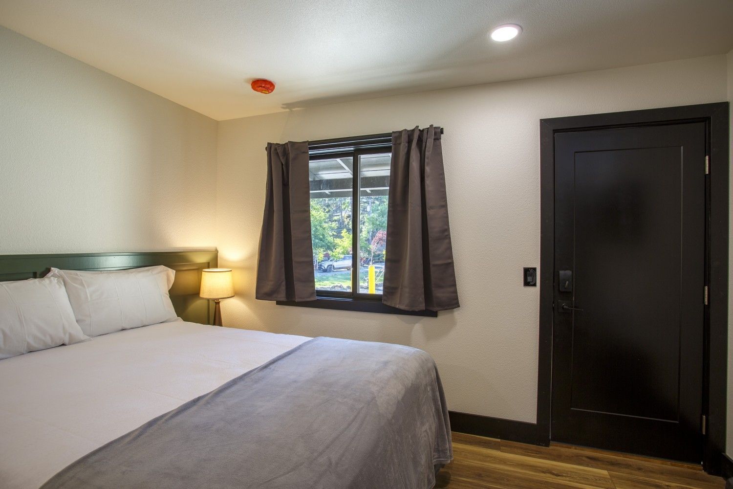 Neat bedroom with a bed, bedside lamp, window with curtains, and a dark closet door
