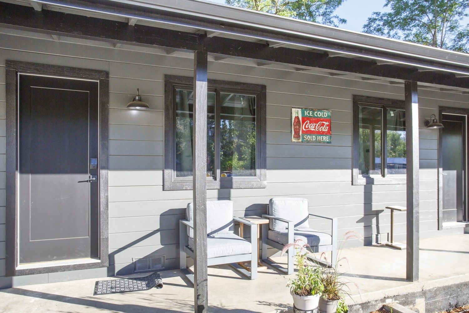Outdoor patio of a small building with chairs, a table, and a red “Open” sign by the door.