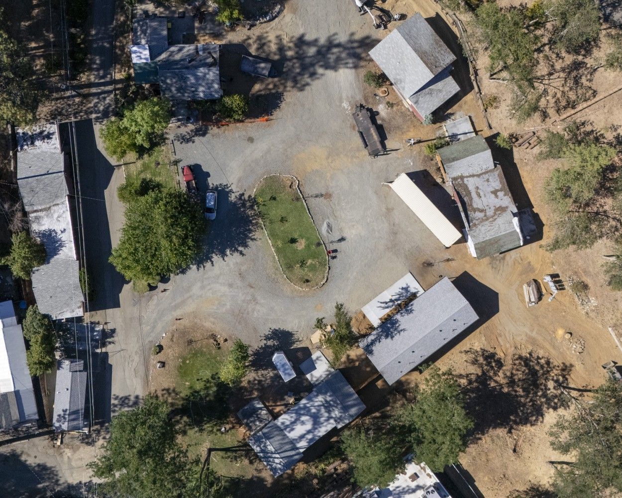 Aerial view of a small rural compound with several buildings, trees, and a dirt courtyard.