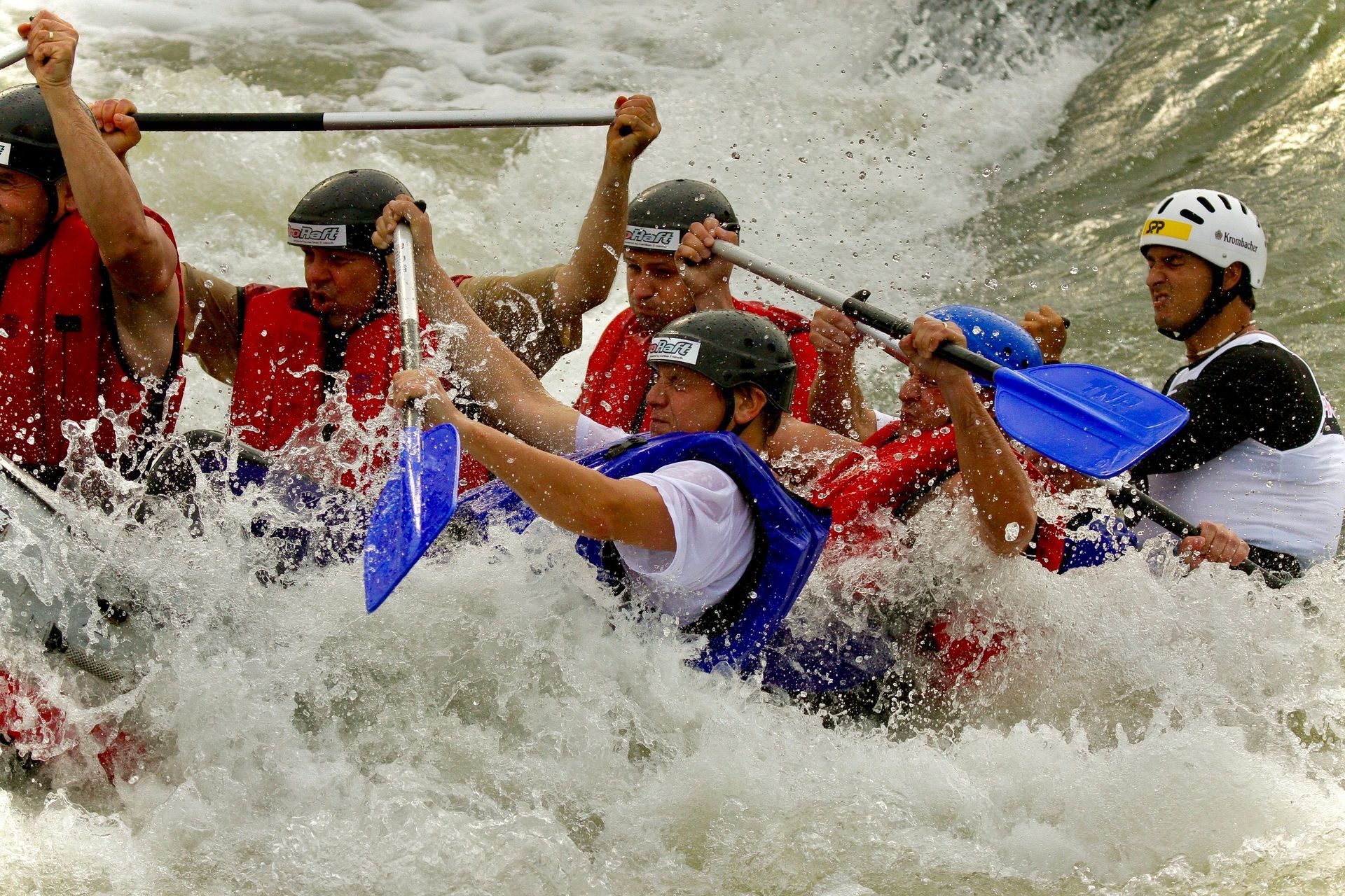 Whitewater rafters in helmets paddling through churning rapids, splashing water everywhere