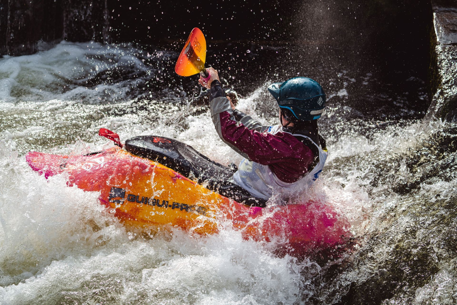 Kayaker in a red raft paddling through rushing whitewater spray