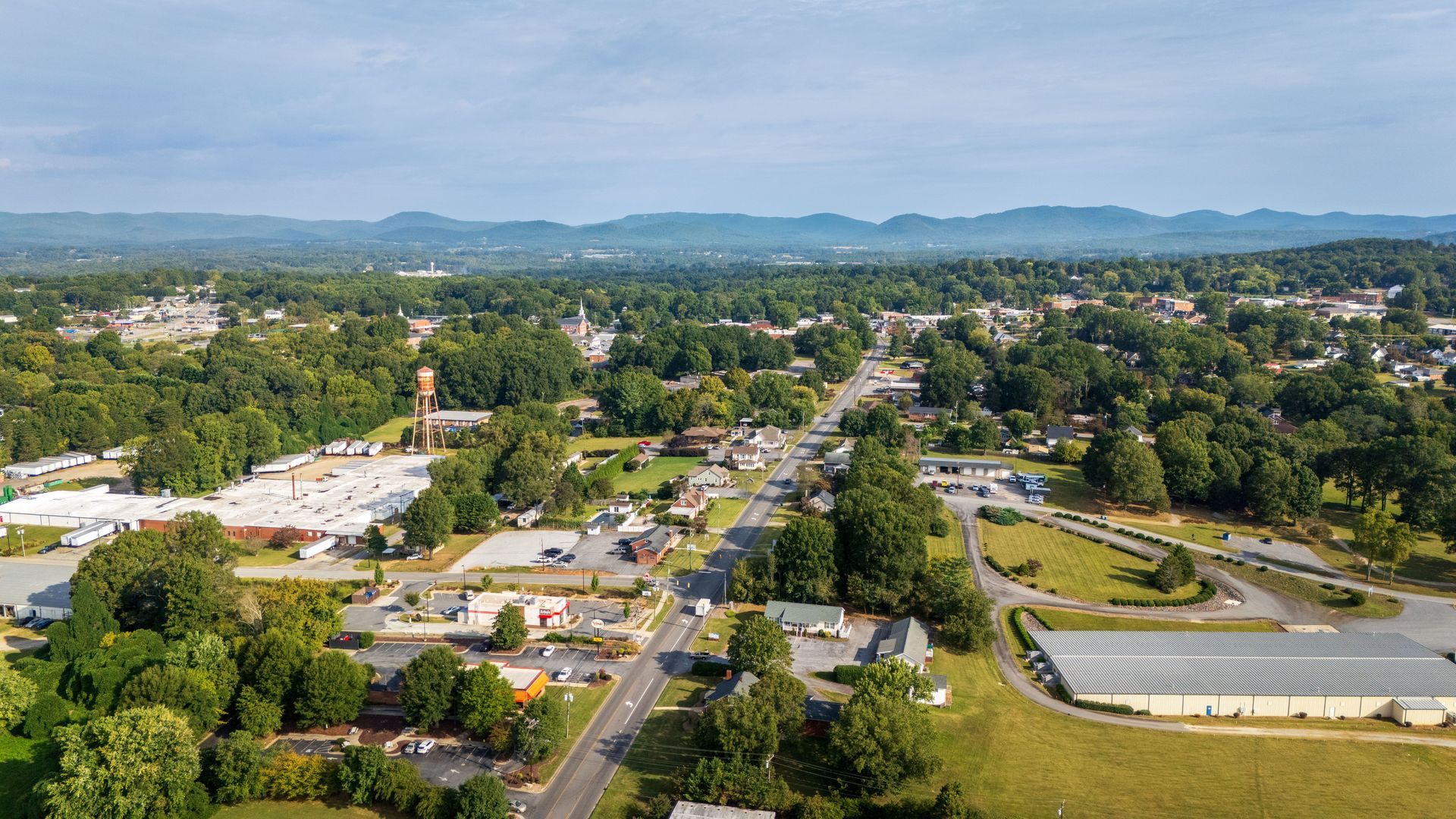 Aerial view of a suburban neighborhood with roads, houses, trees, and distant mountains under a clear sky