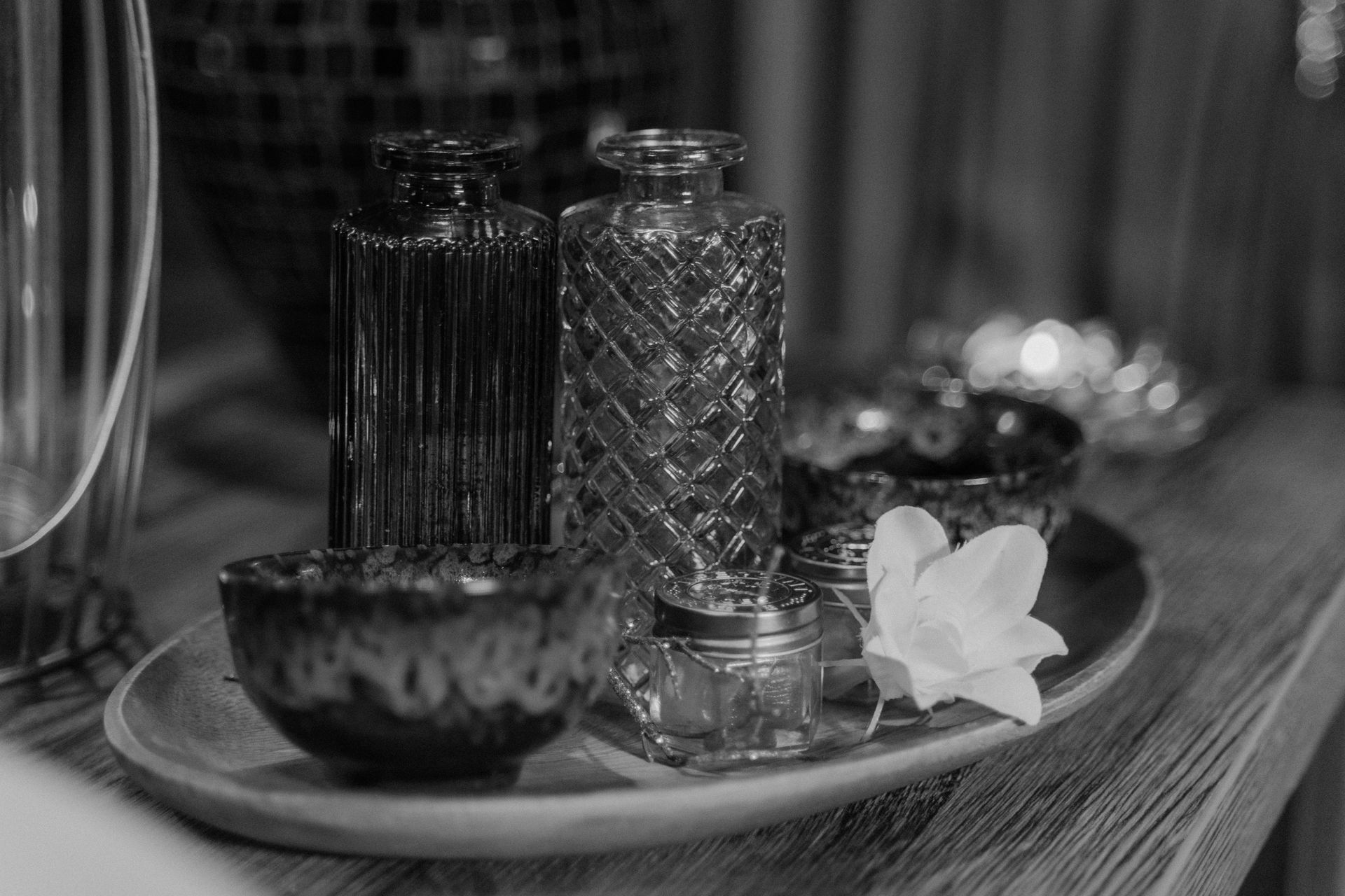 Black-and-white still life of glass bottles, a bowl, and a white flower on a tray