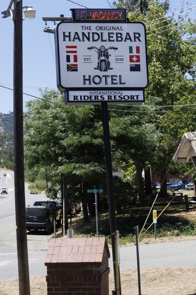 Handlbar Hotel roadside sign reading “The Original Handlebar Hotel” and “Rider’s Resort” amid trees.
