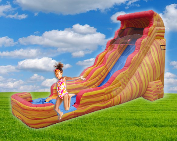 Child on a colorful inflatable slide in a grassy field under a blue sky with clouds