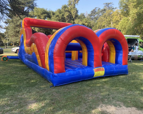 Red and blue inflatable obstacle course on grass in a park-like setting