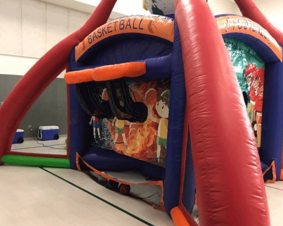 Red and blue inflatable basketball game booth indoors with orange trim and hoop openings