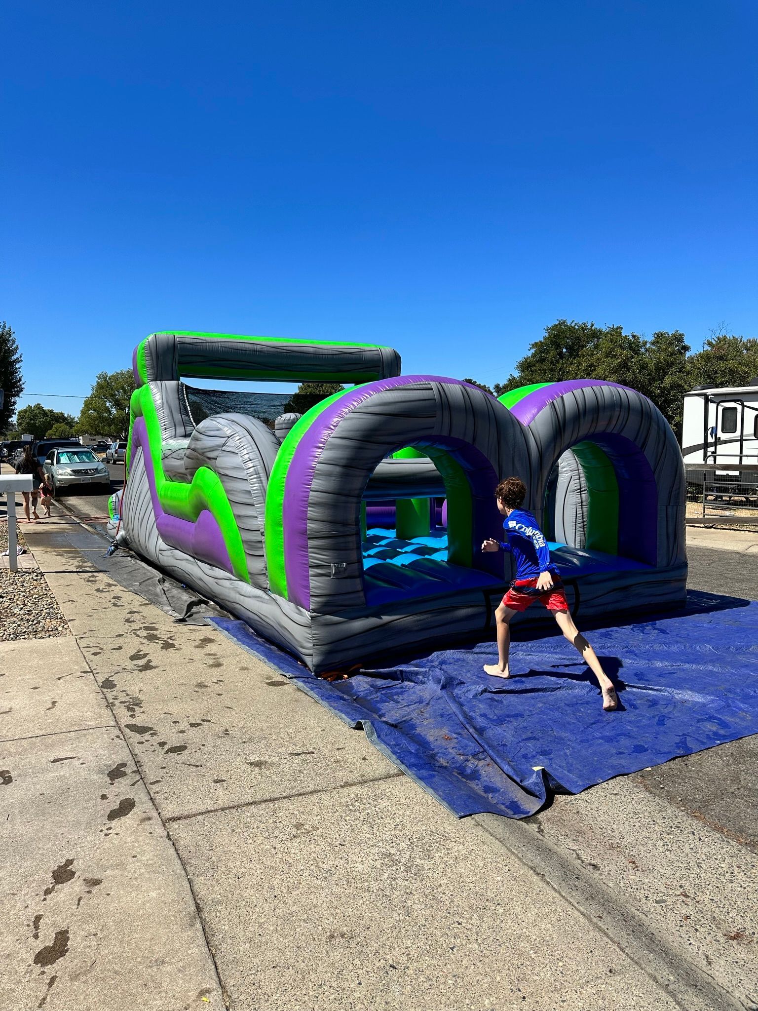 Inflatable obstacle course with a child crawling on blue mat under a bright blue sky