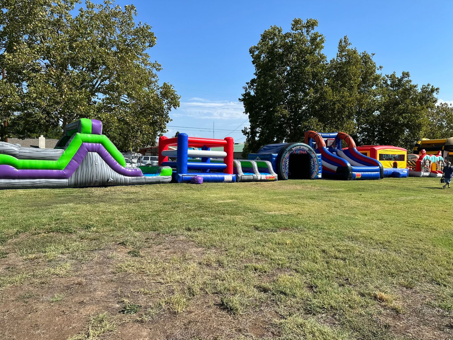 Colorful inflatable bounce houses and slides lined up on a grassy field under a clear blue sky.