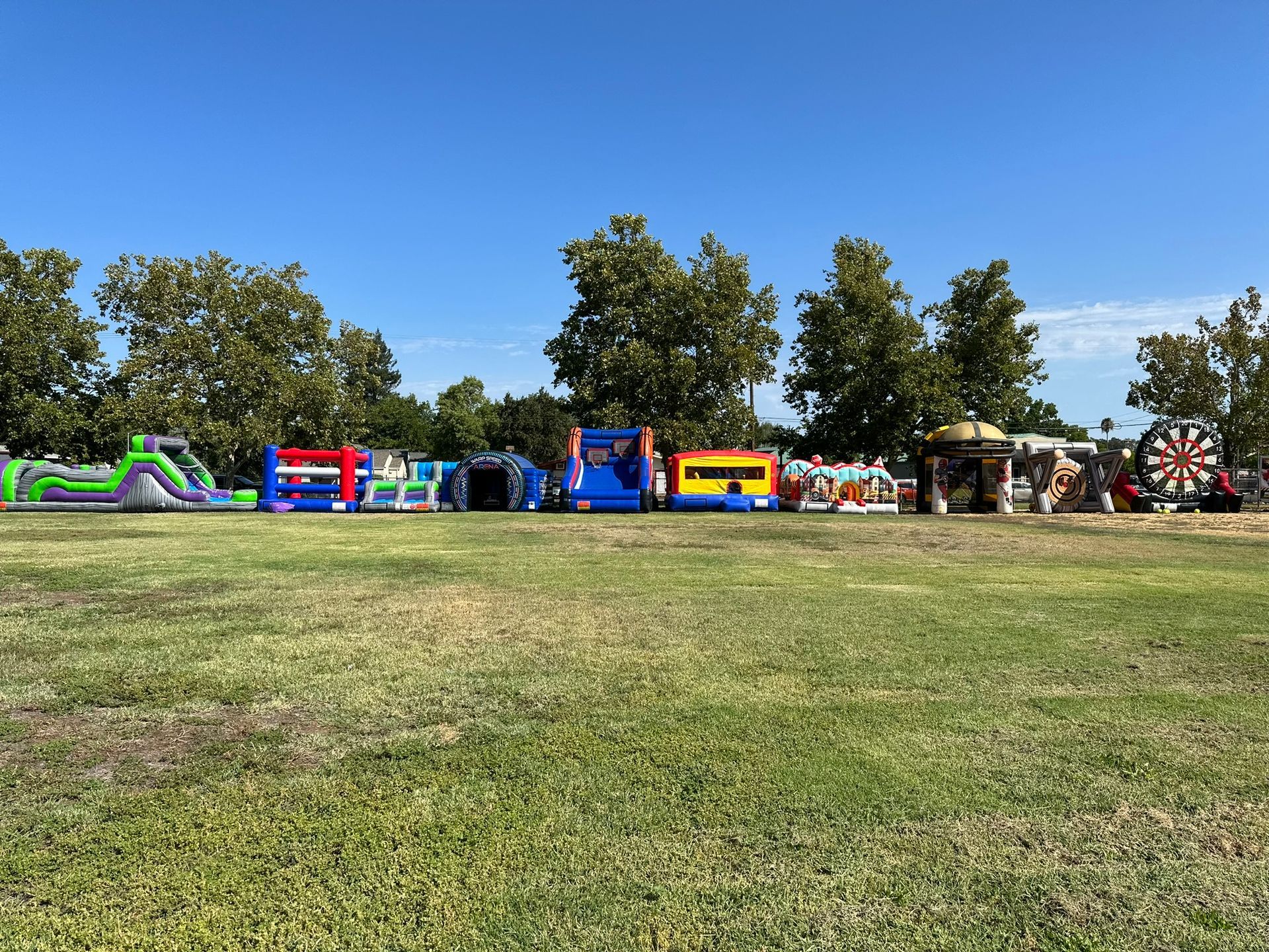 Inflatable carnival rides and booths on a grassy field under a clear blue sky