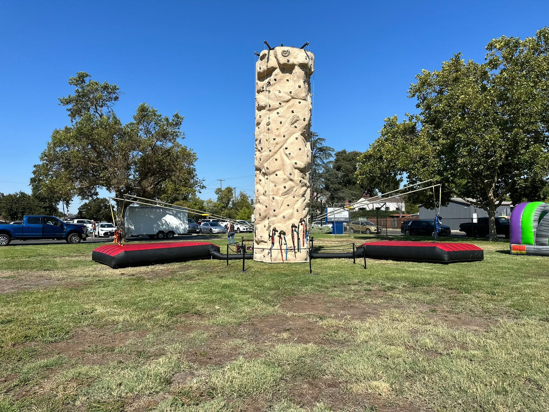 Outdoor climbing wall with red and black crash mats in a grassy park on a sunny day