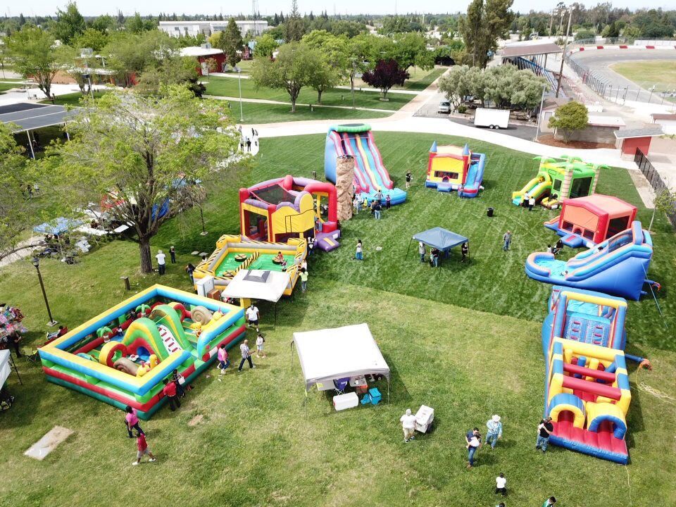 A park with colorful inflatable bounce houses and slides on a grassy field, with a few people nearby