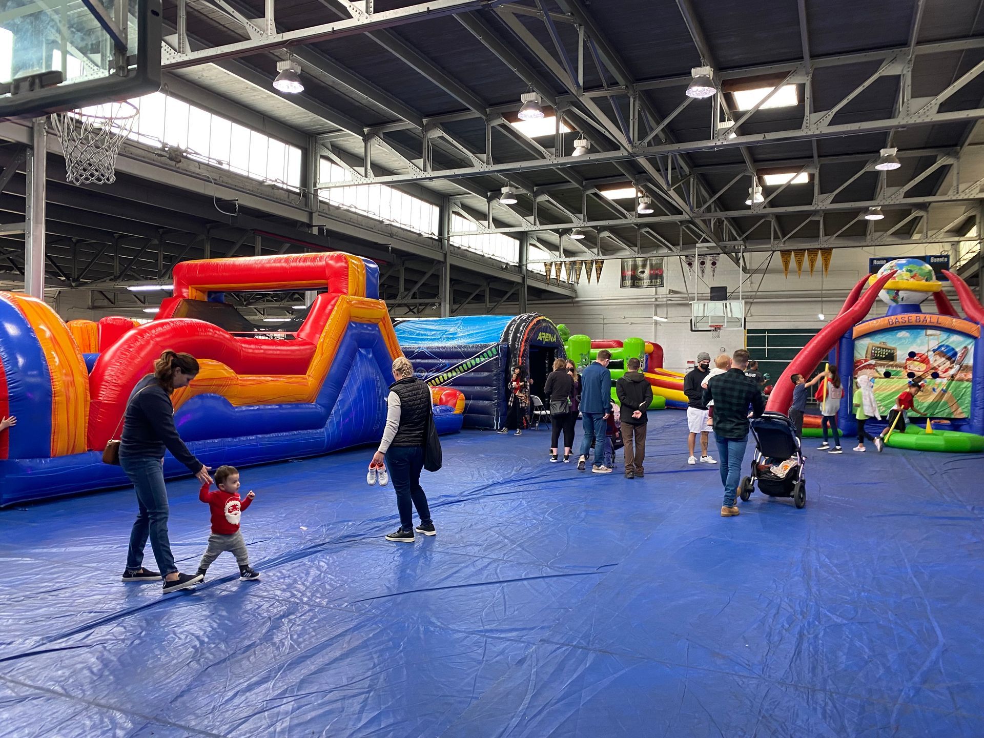 Indoor bounce house event with children playing on colorful inflatables in a large gymnasium