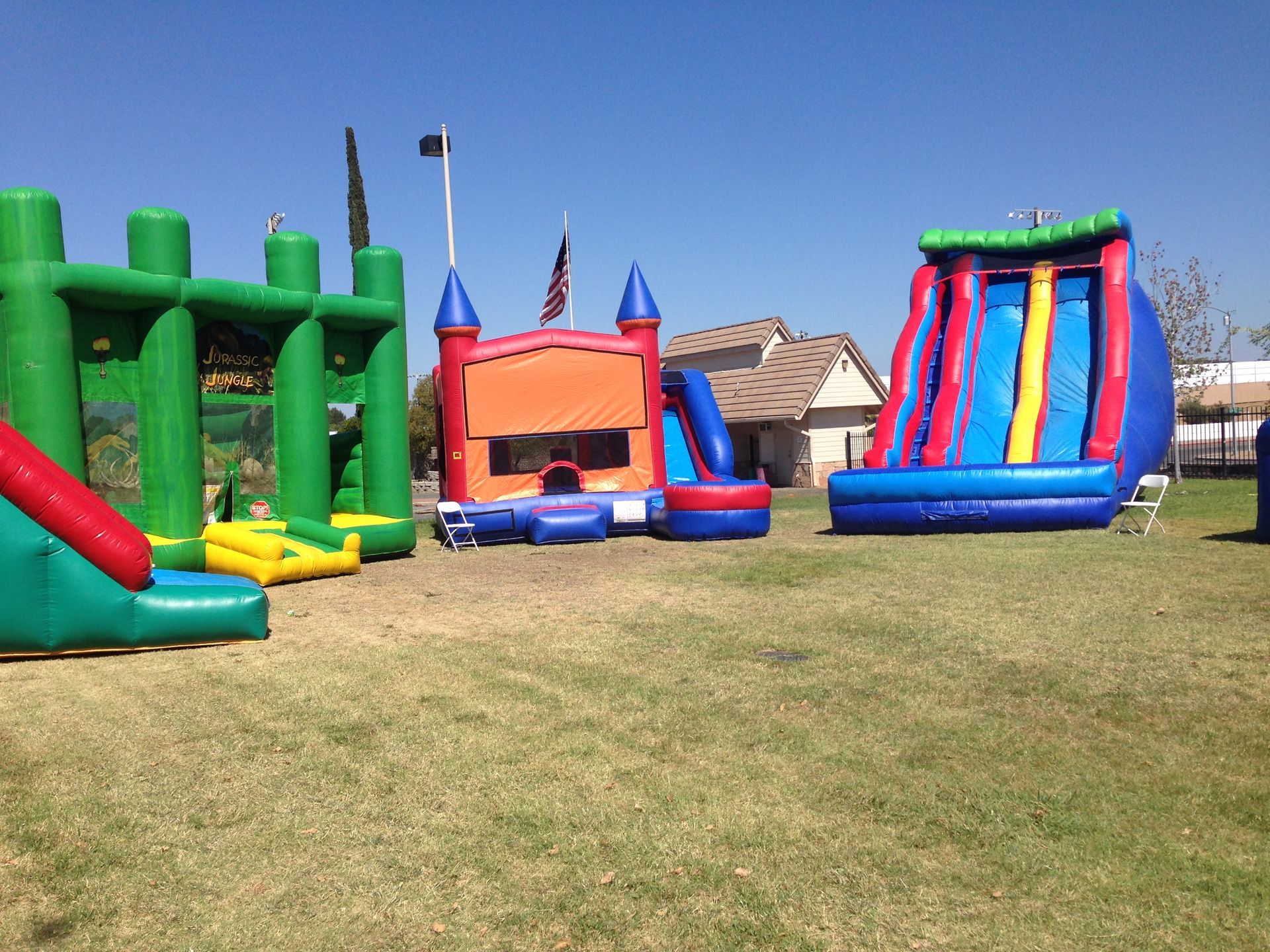 Colorful inflatable bounce houses and slides set up on a grassy field under a clear blue sky.