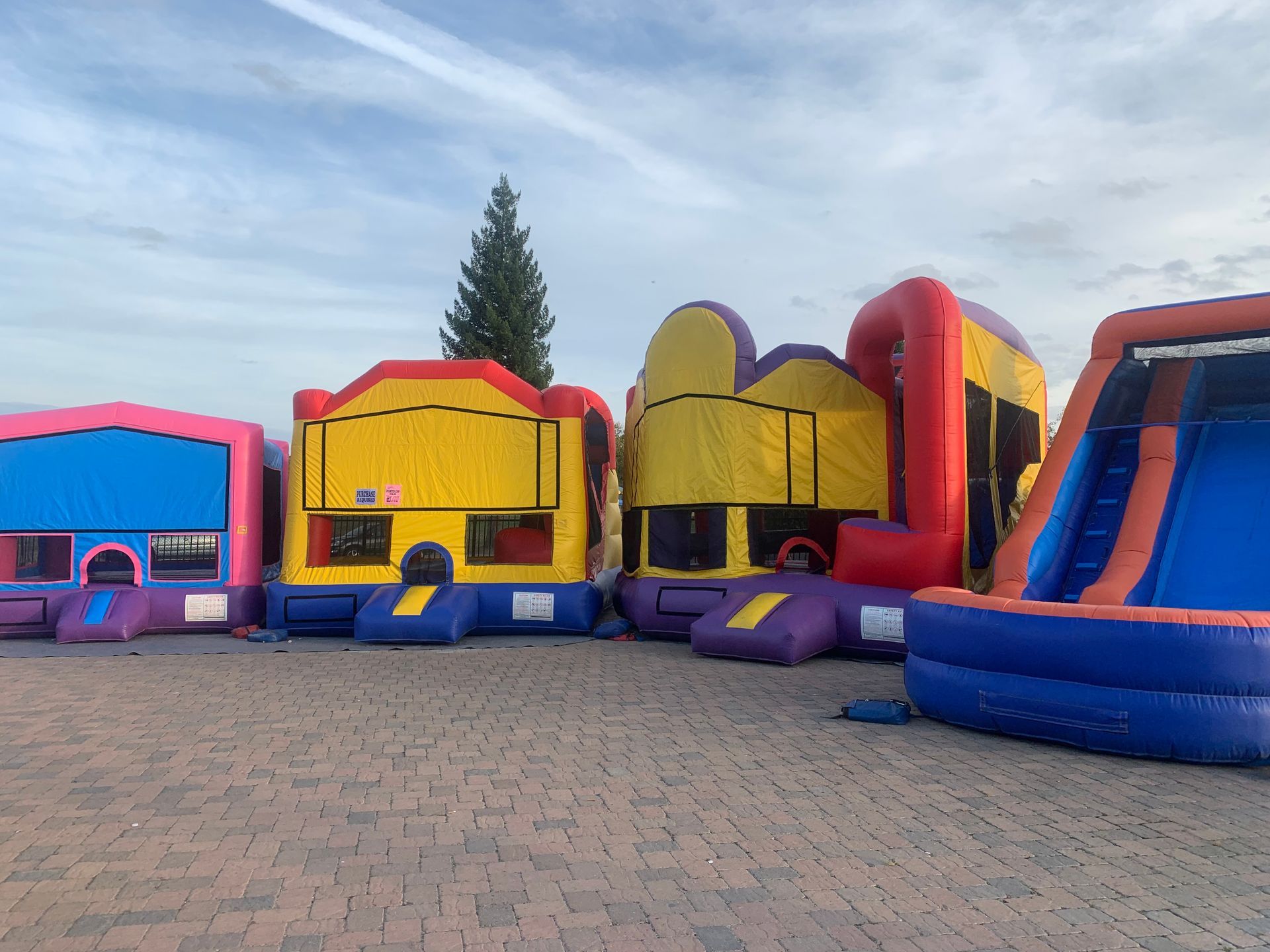 Colorful inflatable bounce houses lined up on a brick plaza under a cloudy sky.