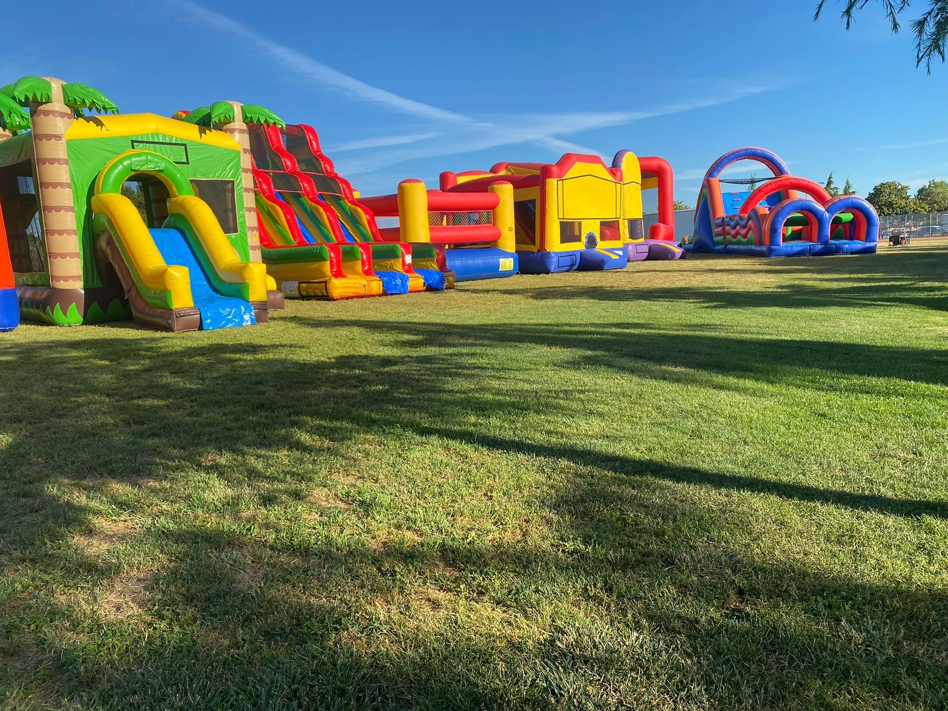 Colorful inflatable bounce houses and slides on a grassy field under a blue sky
