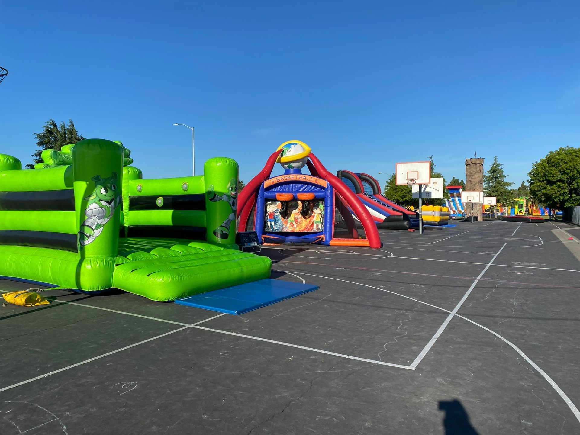 Colorful inflatable obstacle course and bounce house on an empty paved lot under a clear blue sky