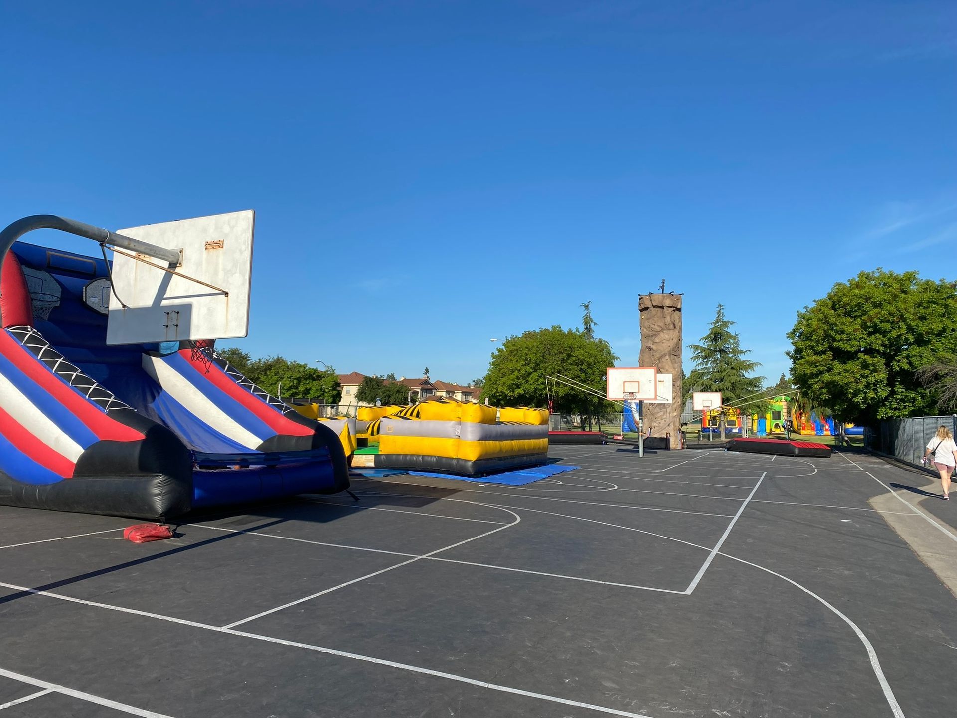Empty outdoor fairground with inflatable slides, basketball hoops, and a clear blue sky.