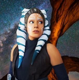 Woman in a striped blue-and-white headpiece, looking left against a starry sky and tree trunk backdrop