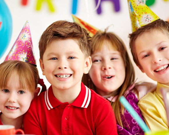 Children in colorful party hats smiling at a birthday celebration