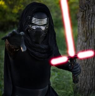 Masked figure in black wielding a red crossguard lightsaber in a wooded area