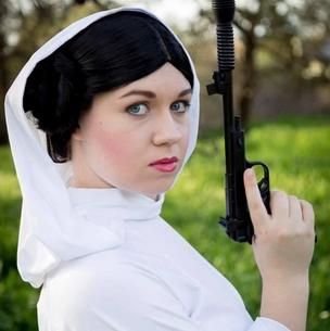 Person in a white outfit holding a black pistol near a green outdoor background