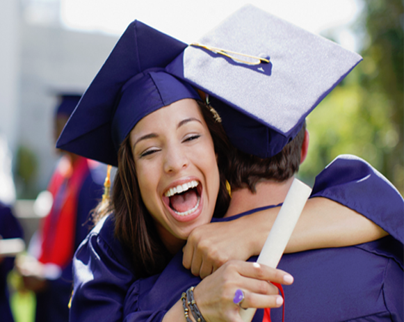 Two graduates in purple caps and gowns hugging, one smiling broadly and holding a diploma