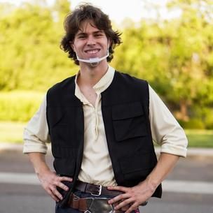 Smiling person in a black vest and cream shirt standing outdoors with hands on hips