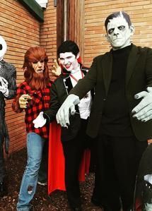 Halloween-costumed people posing by a brick wall, including a Frankenstein character in front.