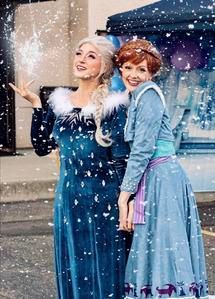 Two women in blue winter dresses posing in falling snow with umbrellas