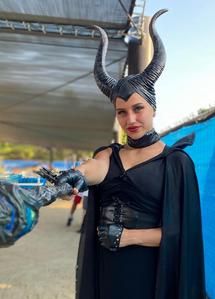Person in a black Maleficent-style costume with horned headpiece holding a prop under a canopy.