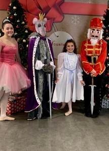 Three children in holiday costumes posing indoors beside a Christmas tree and giant nutcracker